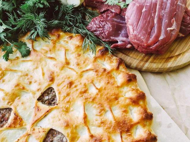 A golden-topped Australian beef and mushroom pie, one cut open to show the rich, chunky gravy filling.
