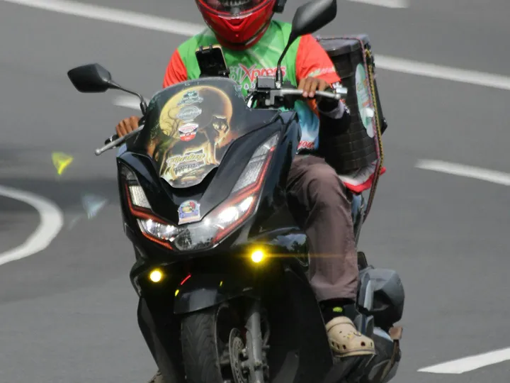 A motorcycle rider with an insulated delivery box riding through a Vancouver neighbourhood.