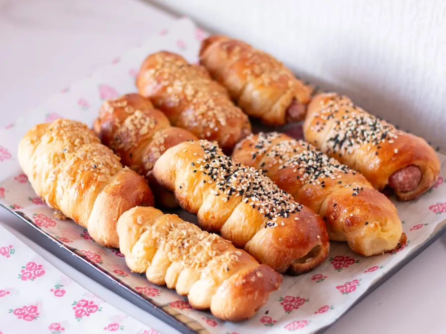 Two flaky golden pork and fennel sausage rolls on baking paper, the puff pastry shattering.